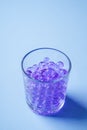 Purple marbles in drinking transparent glass blue background angle view Royalty Free Stock Photo