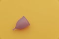 Purple menstrual cup on a yellow background with copy space. Women's hygiene, menstruation, critical days