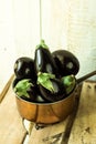 Purple mini eggplants in a copper dipper on vintage wood box on white background,top angle view