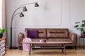 Purple pillow and pastel pink blanket placed on leather couch in real photo of bright sitting room interior with metal lamp, coffe Royalty Free Stock Photo