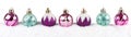 Purple, pink & turquoise Christmas baubles in snow isolated