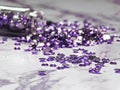 Purple rhinestones poured from a glass bottle on a marble table