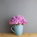 Purple rose flowers in ceramic cup on wooden table with gray background Royalty Free Stock Photo