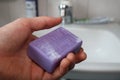 Purple soap bar in a hand. Bathroom sink in background Royalty Free Stock Photo