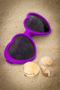 Purple sunglasses in shape of heart with shells on sand Royalty Free Stock Photo