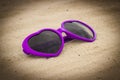 Purple sunglasses shaped heart on the sand Royalty Free Stock Photo