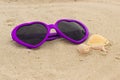 Purple sunglasses shaped heart with shells on the sand Royalty Free Stock Photo