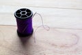 Purple thread spool and sewing needle with copy space isolated on wooden background closeup Royalty Free Stock Photo