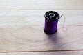 Purple thread spool and sewing needle with copy space isolated on wooden background closeup Royalty Free Stock Photo
