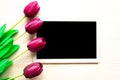 Purple tulips and black mockup tablet on wooden background.