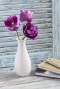Purple tulips in a white ceramic vase and a stack of books on a blue rustic wooden background Royalty Free Stock Photo