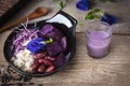 Purple vegetable salad in black bowl placed on the wood table there are spoon, black rice, salad dressing and flower placed around