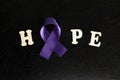 Purple or violet ribbon color on dark black background with word hope. National cancer prevention month. Royalty Free Stock Photo