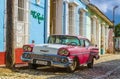 Purple and white classic American car and blue colonial building in streets of Trinidad