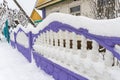 Purple and white concrete carved fence covered with snow, village house, snowy winter