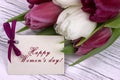 Purple and white tulips with white paper on a white wooden background and card lettering happy women`s day english. Womans Day. 8 Royalty Free Stock Photo