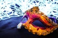 Purple and yellow carnival mask on black silk. There are festive white lights in the background. Royalty Free Stock Photo