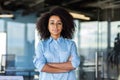 Purposeful black woman wearing blue shirt and round eyeglasses and standing wit folded on chest arms indoors. Confident Royalty Free Stock Photo