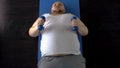 Purposeful fat man lifting dumbbells with great effort lying on mat, top view