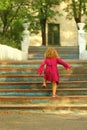 Purposeful toddler girl in pink dress reaching the top of old blue vintage stairs