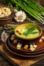 Purred creamy asparagus soup in glass bowl on black plate against raw fresh asparagus and greenery Royalty Free Stock Photo