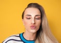 Pursed lips of trendy woman while make a selfie, amused girl wants to kissing, isolated on yellow background