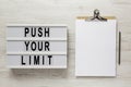 `Push your limit` words on a lightbox, clipboard with blank sheet of paper on a white wooden surface, top view. Overhead, from