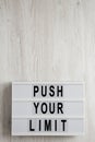 `Push your limit` words on a lightbox on a white wooden background, top view. Overhead, from above, flat lay. Copy space