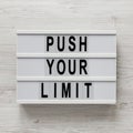 `Push your limit` words on a lightbox on a white wooden surface, top view. Overhead, from above, flat lay. Close-up