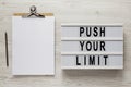 `Push your limit` words on a modern board, clipboard with blank sheet of paper on a white wooden surface, top view. Overhead, fr