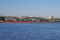 A pusher tugboat pushes two empty barges along the riverbank in a town on the Volga