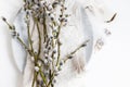 Pussy willow branches and feathers on modern plate on napkin on white wooden table. Top view. Modern Easter table decoration.