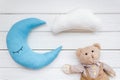 Put baby into bed with moon pillow, clouds, teddy bear and toy on white wooden background top view Royalty Free Stock Photo