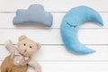 Put baby into bed with moon pillow, clouds, teddy bear and toy on white wooden background top view