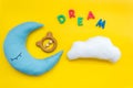 Put baby into bed with moon pillow, clouds, toy and dream copy on yellow background top view