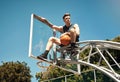 Put in the effort to make your dreams come true. a sporty young man sitting on a basketball hoop on a sports court.