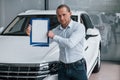 Put your text here. Manager stands in front of modern white car with paper and documents in hands Royalty Free Stock Photo