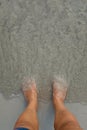 Putting man feet inside the water wave on a sandy beach Royalty Free Stock Photo