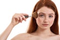 Putting some makeup. Portrait of half naked cute red-haired woman with freckles holding makeup brush and looking at Royalty Free Stock Photo