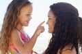 Putting on sunblock. A young girl poking her mothers nose while theyre at the beach.