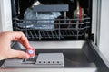 A man hand holding dishwasher detergent tablet. Putting tab into dishwasher, close up.  Dishwasher machine full loaded Royalty Free Stock Photo