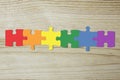 Puzzle with 6 pieces with the colors of the lgtb flag joined together. wooden background