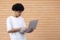 A puzzled African-American guy holding an open laptop and looking into it, writing a message to his team Royalty Free Stock Photo