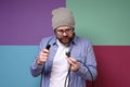 Puzzled bearded man, in round glasses and a hat, with a serious look looks at the plug with a wire, which he holds in Royalty Free Stock Photo