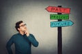 Puzzled businessman keeps hand under chin, thoughtful gesture, looking up at a signpost with arrows showing past, present and