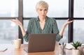 Puzzled Businesswoman At Laptop Gesturing Sitting In Modern Office