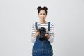 Puzzled confused brunette female photographer with two hairbuns wearing denim overall using modern camera. Woman with