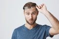 Puzzled and confused male student with stubble dressed in blue t-shirt, looking at camera with blue eyes, thinking about