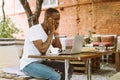 Puzzled and confused multicultural dark skin man using laptop, sit in cafe outdoors, looking at monitor. Job interview Royalty Free Stock Photo