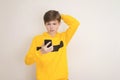 Puzzled, confused teenager boy in yellow hoodie sweatshirt with smartphone